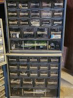 Front view of two stacked black plastic storage units with multiple small clear drawers containing assorted fasteners and hardware items, some labeled.