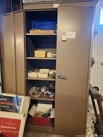 Wide shot of the metal two-door storage cabinet with one door open, showing items stored inside on shelves.