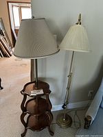 Front view showing 3-tier wooden table with built-in lamp next to brass floor lamp, both with beige pleated lampshades.