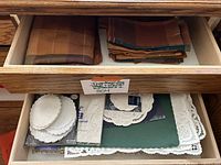 Drawer with assorted placemats and a variety of white paper doilies with scalloped edges.