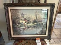 Framed print depicting an English countryside scene with cottage reflected in pond and ornate dark wood frame.