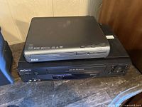 Stacked Sony VCR and RCA DVD player on table, front view showing input/output ports and buttons.