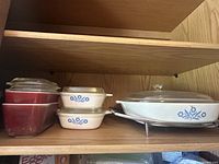 Shelf with all dishes grouped together, showing large oval Corning Ware dish with metal stand, two small square Corning Ware bowls with lids, and two red Pyrex bowls.