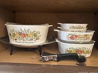 Seven-piece set including a large CorningWare casserole, three smaller bowls, a medium glass-lidded bowl, chrome chafing dish, and handle arranged on shelf.