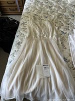 Full view of vintage chiffon nightgown laid flat on floral mattress showing straps, bodice with lace detail and pleated skirt