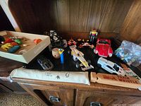Wide-angle view showing vintage toy cars, mechanical figures, a wooden train whistle, assorted small toys, and plastic marbles in bags on wooden cabinet.