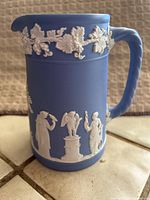 Front side of small Wedgwood Jasperware pitcher showing white grapevine band near top and white classical figures around the body.