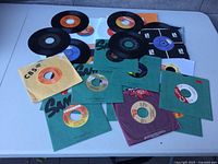 Overview of approximately 30 45 RPM records with assorted sleeves and labels laid on table