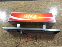 Front view of illuminated Coca-Cola sign showing logo panel and metal housing