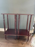 Pair of matching cherry stained wooden plant stands side by side, showing turned legs and lower shelves.