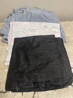 Three fabric pieces stacked: light blue on top, white patterned in the middle, black on the bottom; placed on a beige surface.