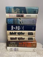 Photo of eight hardcover novels stacked upright showing titles and authors.