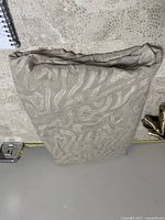 Folded beige fabric with raised pattern and sheen on patterned surface