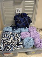 Open view of Rubbermaid container revealing yarn skeins inside in various colors: solid light blue, purple, black and blue, twisted black/white/navy blue.