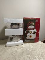 Full view of the snowman cookie jar in original box with Styrofoam padding on top and bottom for protection.