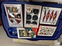 Multiple boxed sets of Christmas tree ornaments in various colors and styles on a blue plastic bin lid
