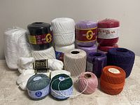 Photo displaying an assortment of crochet cotton yarn rolls and skeins in various colors arranged on a flat surface.