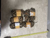 Five skeins of novelty yarn on a surface with a measuring tape alongside for scale.