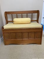 Front view of solid wood deacon's bench with yellow seat cushion and bolster pillow on carpeted floor.