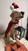 Front right angled view of dog figurine with Santa hat and cape holding a black metal lantern.