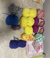 Overview of multiple yarn skeins in assorted solid and variegated colors arranged on textured surface.