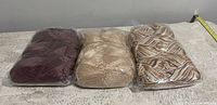 Three balls of yarn in plastic packaging laid out side by side showing color and packaging.