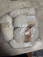 Nine rolls of Patons Cotton Top yarn in off white, packaged together in clear plastic.