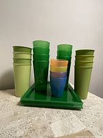 Eight tall green plastic glasses, four smaller kids plastic glasses in various colors, arranged on charger plates.