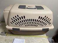 Full view of beige and brown plastic pet carrier with ventilation holes measuring length with tape measure showing approx 22 inches.
