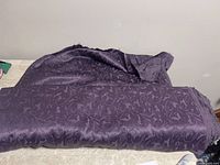 Bolt of purple fabric with decorative floral pattern shown folded on table.