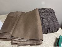 Photo showing two pieces of brown tone fabric; smooth raw silk and a crinkled sheer material, folded and laid flat on a surface.