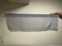 Full length of the sheer grey fabric rolled out horizontally and held by hand to show fabric's texture and color.