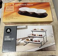Photo shows two boxed serving sets: Home Collection Maison condiment server with wooden tray, and hometrends 3-tier stoneware serving set.