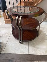 Front angled view of the round wooden side table with glass insert and metal curved handles