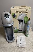 Photo showing SodaStream Fizz home soda machine, CO2 cylinder, original box, and user manual all placed on a gray surface.