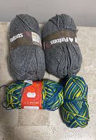 Two grey Patons yarn skeins and two multi-color yarn skeins on a beige surface