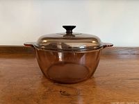 Front view of the amber-tinted glass pot with lid on a wooden surface.