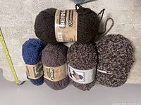 Photo of five skeins of Bernat yarn in various colors on concrete surface with ruler for scale.
