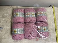 Six rolls of pink yarn arranged in two rows of three on a wooden surface. Three rolls are labeled Master Cotton with a sunflower image, three rolls are unlabeled. Yarn is soft and thick, oriented horizontally with a measuring tape visible.