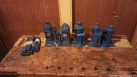 Five blue bottle jacks of various sizes on a wooden surface with metal handles beside them.