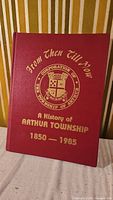 Front cover of the hardcover book titled 'From Then Till Now: A History of Arthur Township 1850-1985' with gold embossed lettering and township crest.