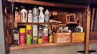 Shelf with assorted cleaning supplies sprays, sealers, rust protection sprays, and wood treatment bottles arranged side by side