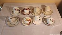 Wide view of all eight cups and saucers laid out on table, showing variety of colors and floral patterns.