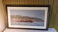 Front view of the framed oil painting showing rocky shoreline and pine trees