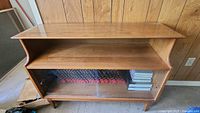 Full front view of midcentury wooden bookcase with upper open shelf and lower shelves enclosed by glass sliding doors. Shows some wear around edges.