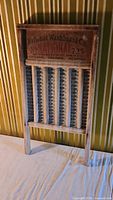 Full view of vintage metal washboard with wooden frame and branded top panel showing age wear.