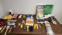 Full overview of painting supplies laid out on table including brushes, roller covers, scrapers, trays, and accessories.