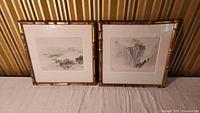 Pair of framed Asian block prints with bamboo style frames and white mats on fabric surface