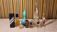 Overview of various perfume and cologne bottles in different sizes and shapes shown on a surface against a striped background.