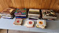 Overview of large stacks of vinyl records including multiple LP albums and 45 RPM singles on a table.